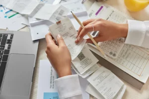 Osoba organizująca paragony przy biurku z laptopem, papierkową robotą i kalkulatorem - zarządzająca finansami lub obliczająca wydatki - rozważająca elektroniczny obieg faktur w celu usprawnienia przetwarzania faktur.